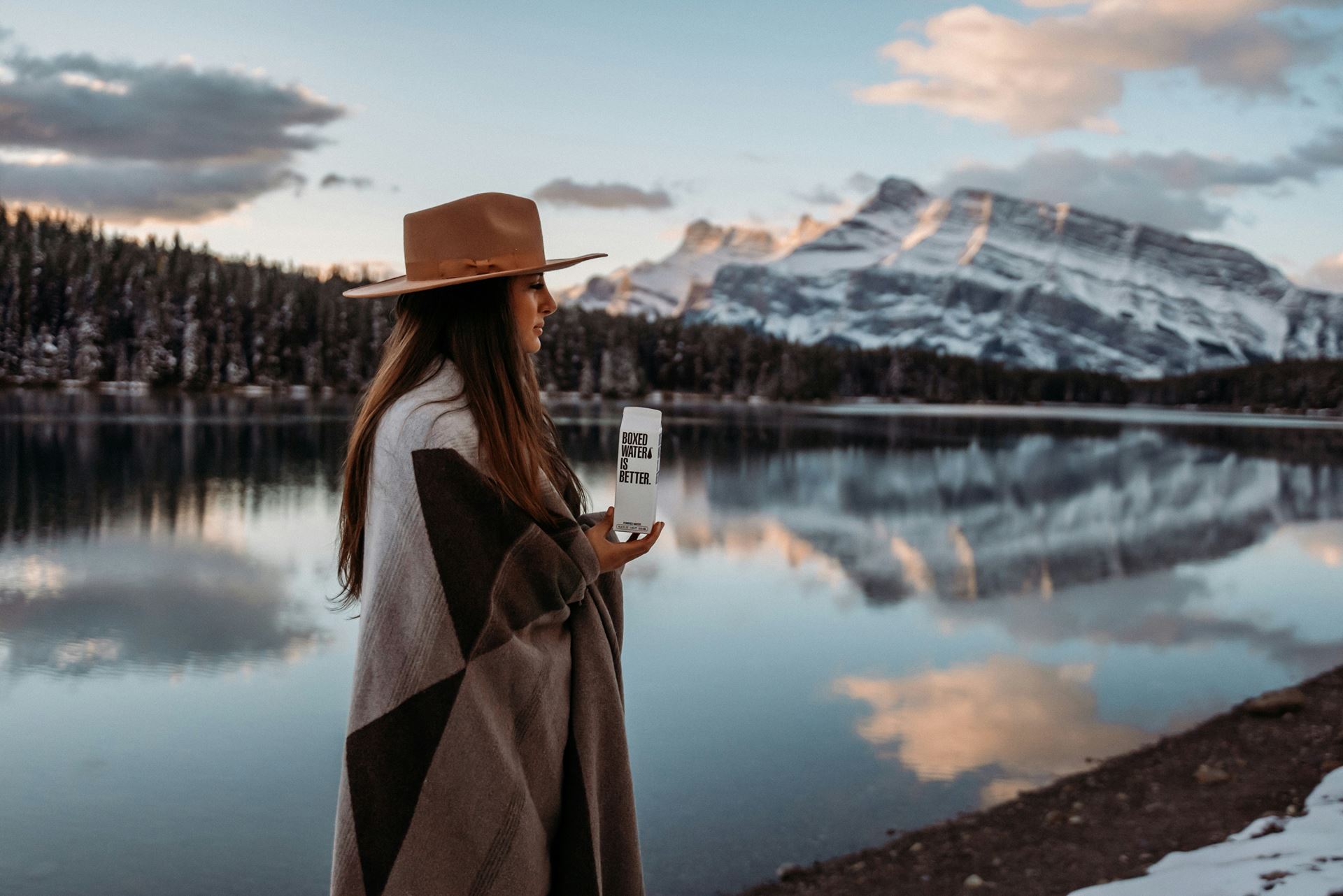 a woman stood outside looking at a lake and mountain scene in winter